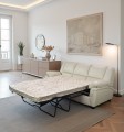 Sofa 3-osobowa, skórzana, z rozłożoną funkcją spania w kolorze jasny beż na tle eleganckiego salonu.